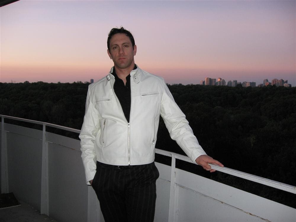 Man in white jacket on balcony overlooking city.